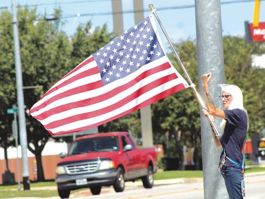 Burnet County resident Laura Silveia raises her arm to encourage the deafening sound of horns as multiple numbers of vehicles motored through the Texas 29 and U.S. 281 intersection Sept. 11. Silveia and 30 others commemorated Patriot Day at the intersection. Photos by Raymond V. Whelan/The...