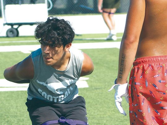 Bentley Trejo uses a band to keep his upper body in place as he runs backwards with his hands behind his back during a defensive back drill.