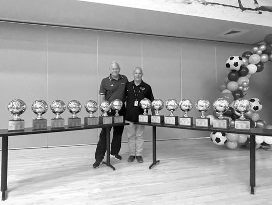 Marble Falls boys soccer assistant coach Chuck Woods (left) and former head coach Rick Hoover with the numerous gold trophies representing the program championships the two have guided the Mustangs to capturing. Contributed photos